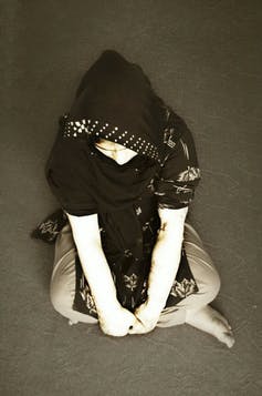 An Afghan women wearing a head covering sits cross-legged on the floor.